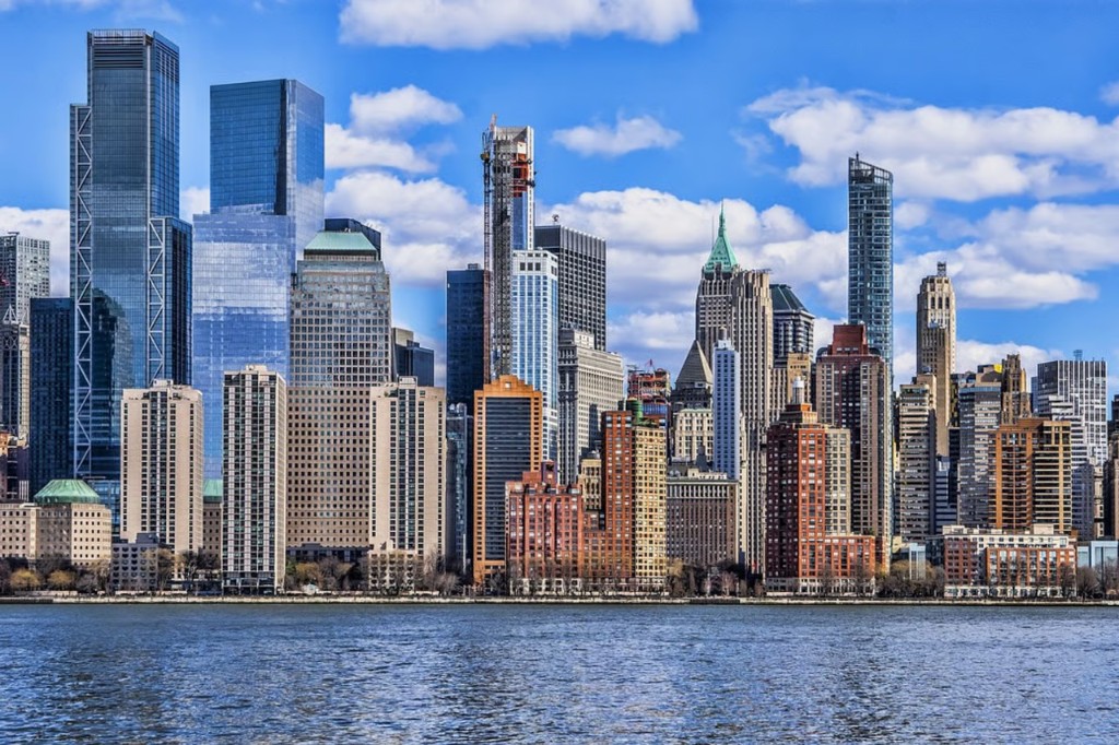 Manhattan skyline across the water under a bright blue sky