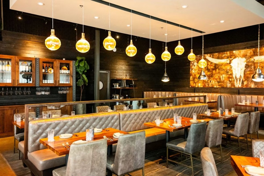 Upscale restaurant interior with tufted banquettes, wood tables, and amber pendant lighting